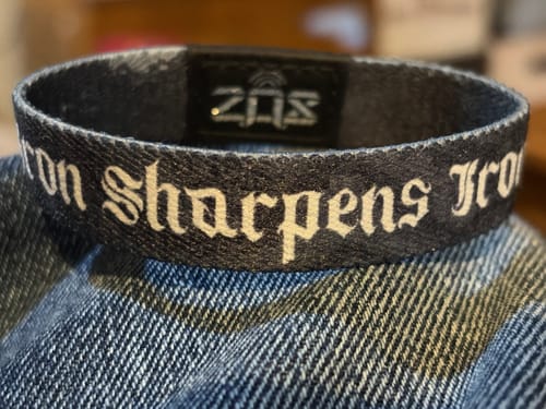 Customer's close-up of the 'Iron Sharpens Iron' bracelet in a dark fabric with white gothic-style text.