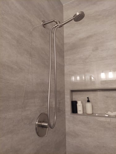 Reviewer's shower system with a handheld shower head installed on a grey tiled wall.