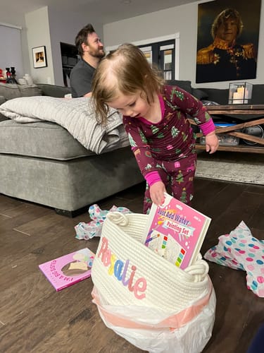 Customer's granddaughter looking into a personalized white rope basket filled with gifts in a living room.