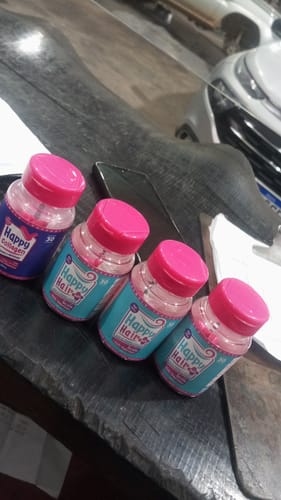 Cliente mostrando os três potes de Happy Hair e um pote de Happy Collagen do kit em uma mesa escura.