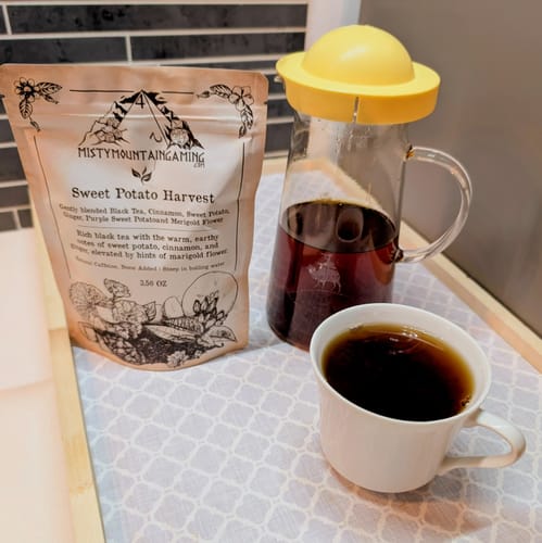 Customer's Sweet Potato Harvest Tea pouch next to a pitcher and mug filled with the brewed, dark tea on a counter.