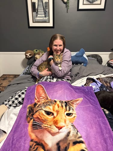 Reviewer holding a cat while showing a purple personalized pet throw blanket with the cat's portrait on it.