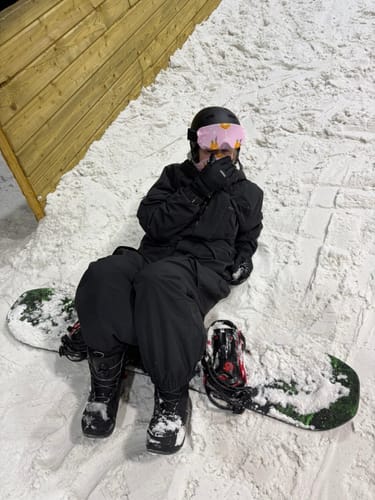 Reviewer sitting in the snow wearing the black techwear multi-pocket insulated snow jacket.