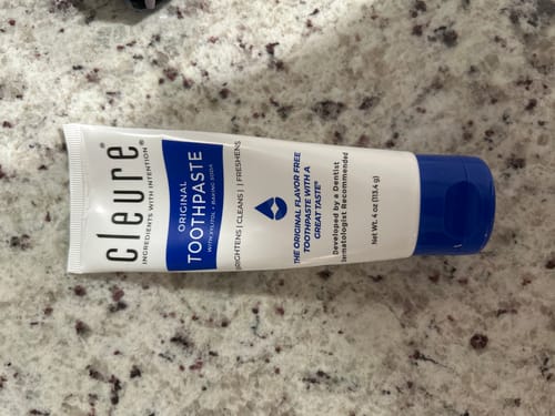Reviewer's tube of Cleure Original Flavor-Free Toothpaste resting on a speckled granite countertop.