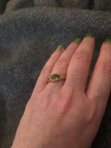 Customer's hand wearing the gold Green Arizona Crystal Ring on their finger against a grey background.