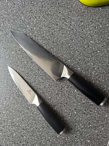 Ein Kunde zeigt zwei Messer des OKAMI-Messersets mit Damastklingen auf einer Arbeitsplatte.