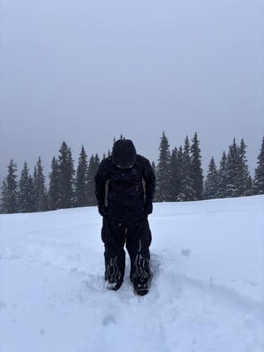 Reviewer wearing the baggy black snow pants with flame details on the cuffs, standing in the snow.