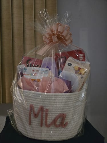 Customer's personalized white woven basket with the name 'Mia', filled with baby items and wrapped with a pink bow.