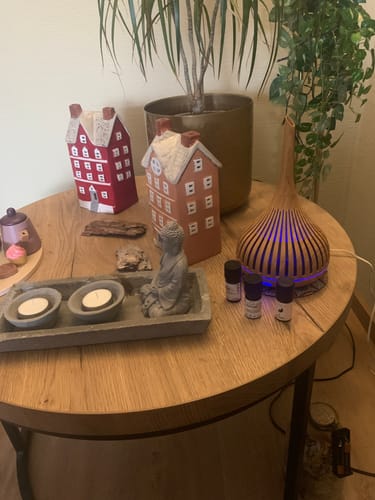Recensent toont de Meditatie etherische olie flesjes in een rustgevende opstelling met een diffuser en decoraties op een houten tafel.