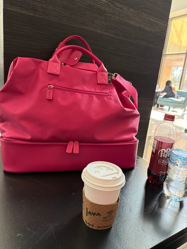 Reviewer's bright pink Weekender Bag on a table in a travel lounge setting, ready for a trip.