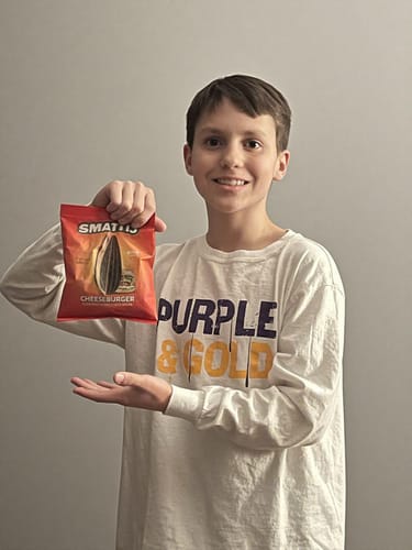 Customer smiling while holding up a CHEESEBURGER LE SINGLE BAG of sunflower seeds.