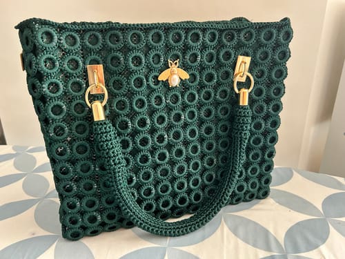 Reviewer's completed dark green Garden Bee Crochet Bag, showing the front with the gold bee embellishment and handle.