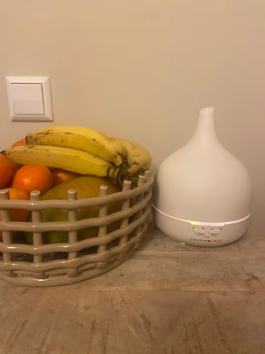 Recensent toont een witte Geurwolkje aromadiffuser die aanstaat naast een mand met fruit.