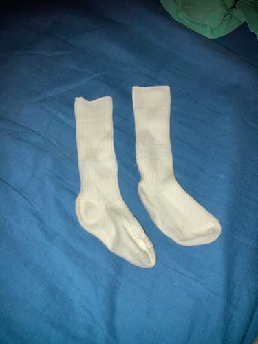 Customer's pair of long, white wool baby socks laid out flat on a blue surface.
