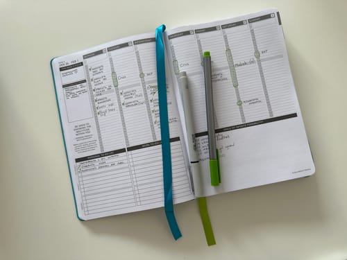 Reviewer's open Starry Jellyfish 2026 Planner showing a filled-out weekly spread, with pens and ribbons marking the page.