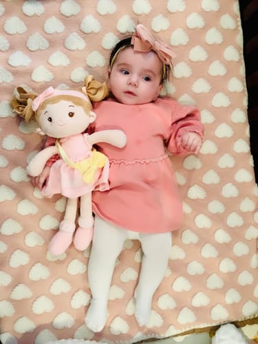 Customer's Personalized Milly Girl doll lying next to a baby on a pink, heart-patterned blanket.