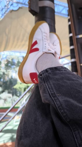 תקריב של לקוח/ה נועל/ת סניקרס Esplar לבנות עם לוגו V אדום וסוליית גומי.