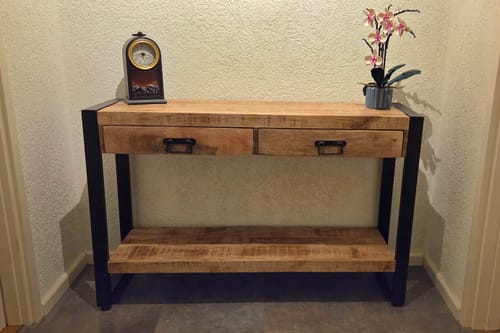 Recensent toont de mangohouten sidetable die perfect in een nis past, met een klok en plant erop.
