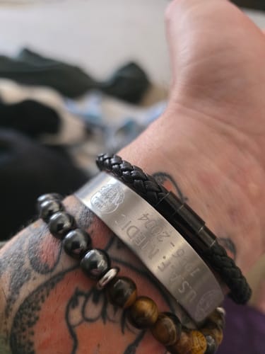 Close-up of a customer's wrist wearing a customized silver bracelet engraved with 'U.S.A.F. MEDIC'.