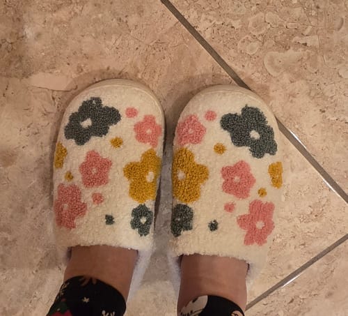 Customer wearing fluffy Livia Flower Slippers with a colorful floral pattern on a tile floor.