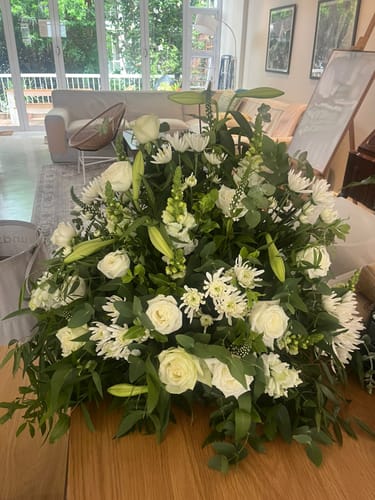 Reviewer's Peace Be With You arrangement of white roses, lilies, and greenery on a wooden table.