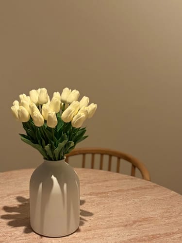 Recensent toont het boeket witte tulpen in een elegante witte vaas.