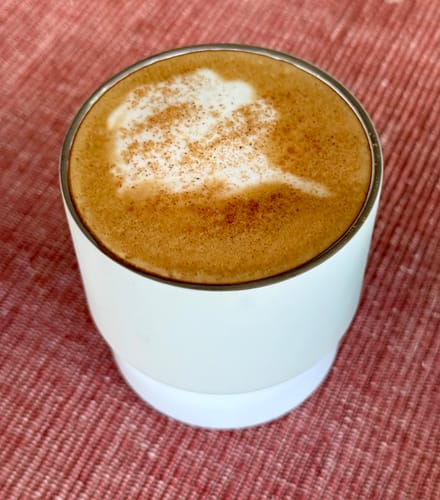 Reviewer's cup of coffee made from Colombian Excelso beans, with creamy foam and cocoa in a white mug.