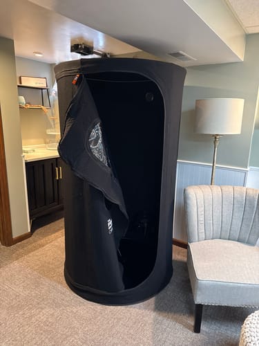 Customer's black Sauna Pod 2.0 assembled in a room with the zippered door partially open.