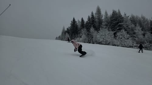 Reviewer snowboarding down a snowy slope wearing the baggy black snow pants.