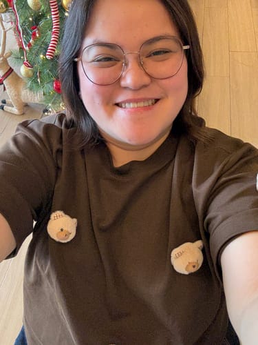 Customer smiling in the Cocoa Brown Teddy Check-Ear Charm T-Shirt, showing the cute plush bear details on the chest.