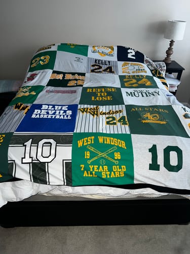 Customer's custom Premium T-Shirt Quilt made from various green, blue, and white sports shirts, laid out on a bed.