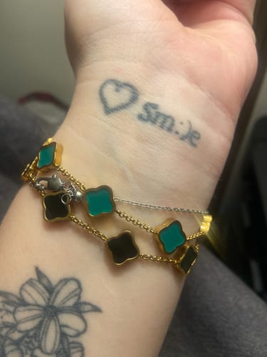 Customer wearing a multi-strand, gold-colored bracelet with black and teal clover charms on their wrist.
