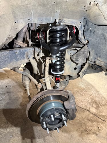 Customer's installed black Upper Control Arms with red bushings on the front suspension of a truck.