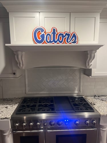 Customer's vibrant Gators 3D metal wall art displayed on a white shelf above a kitchen stove.