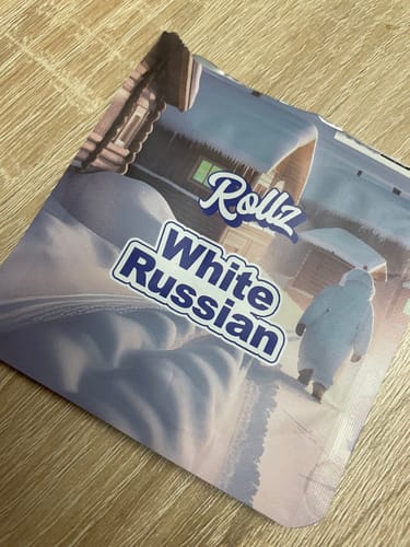 Customer's packaging for the Rollz White Russian THCA Flower, shown on a wooden table.