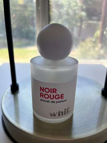 Customer's Noir Rouge perfume in a frosted bottle with a spherical white cap, sitting on a table.