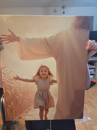 Customer holding their 'The Path of Light' canvas, showing a happy girl running to Jesus's open arms in a sunlit field.