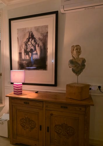 De Grid tafellamp van een recensent, met een rood/paarse geruite voet, staat aan op een houten kast.