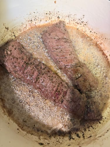 Customer searing two seasoned USDA Choice Outside Skirt Steaks in a white pan.