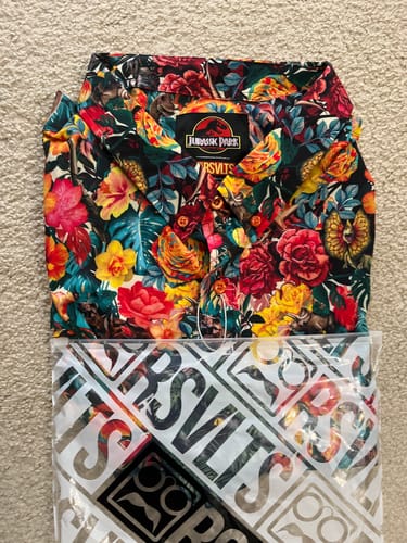 Customer's folded Jurassic Park 'Dinoflor' shirt, showing its vibrant floral and dinosaur print above its packaging.