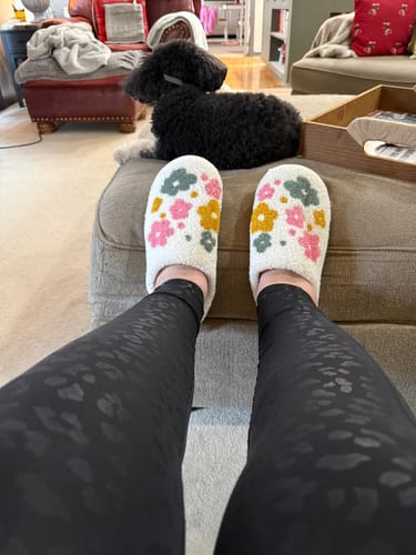 Reviewer wearing the floral Livia Flower Slippers while relaxing with their feet propped up at home.