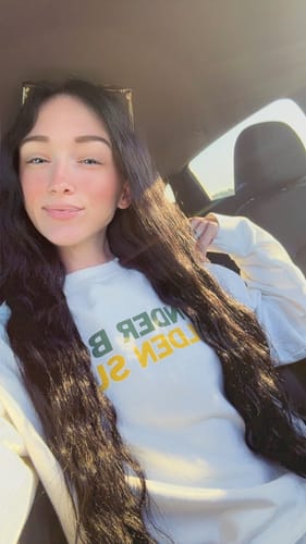 Customer in a car showing off her long, off-black Tape In Hair Extensions, which flow over her shoulders.