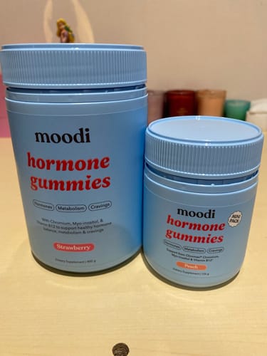 Customer's large tub of Strawberry Hormone Gummies next to a smaller tub of the peach flavor on a table.