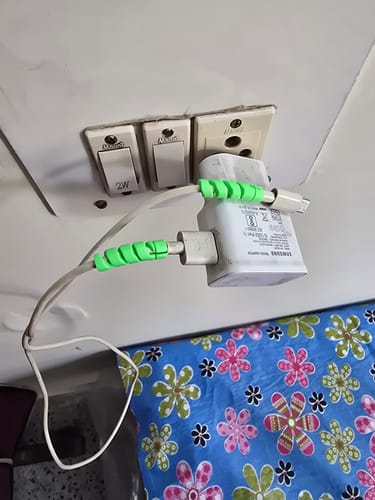 Customer's two green spiral cable protectors attached to a white charging cable plugged into a wall.