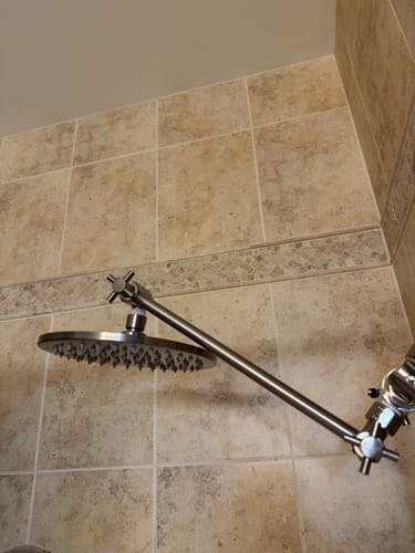 Customer's sturdy adjustable shower arm holding a rainfall showerhead in a tiled shower.
