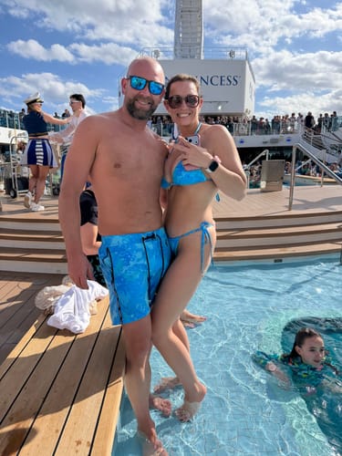 Customer wearing a blue Splatter Bikini Top with her partner in matching swim trunks, posing by a pool on a cruise ship.