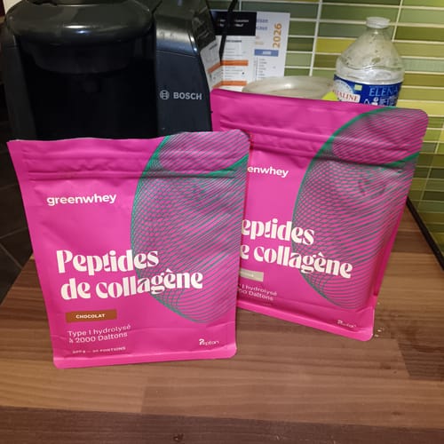 Deux sachets roses de Peptides de Collagène d'un client, saveur chocolat, posés sur un comptoir de cuisine.