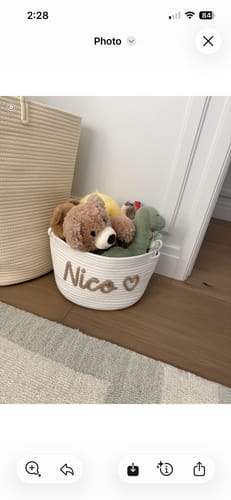 Customer's white Personalized Knitted Basket with 'Nico' and a heart icon, filled with soft toys in a nursery.