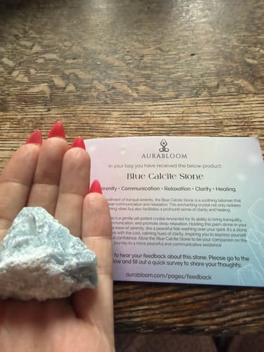 Customer holding the light blue Blue Calcite stone from the VIP Crystal Club with its information card.