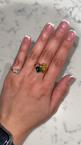 Reviewer's hand wearing the gold Pia Ring on the pinky finger, styled with two other colorful rings on the ring finger.